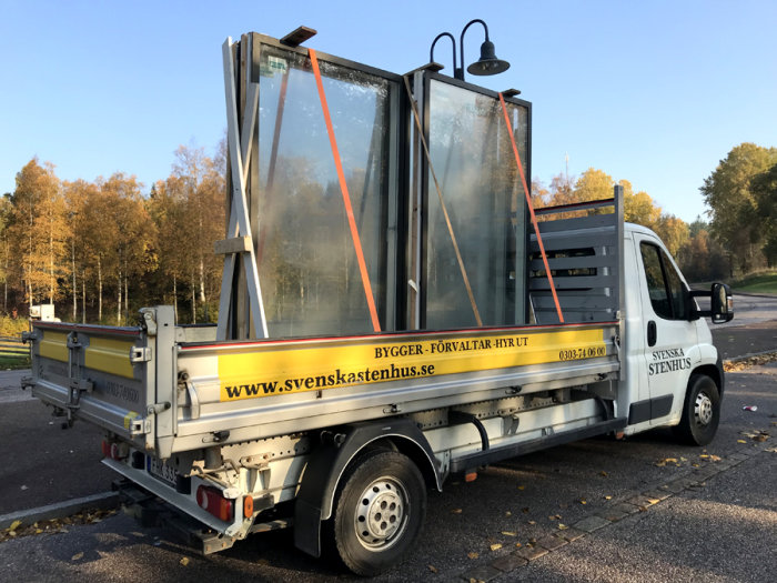 Flakbil som transporterar stora glaspartier, med en företagslogotyp på sidan.