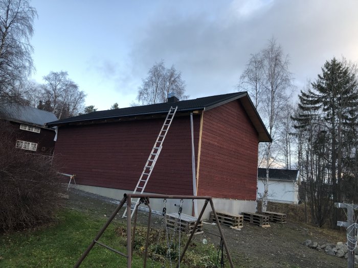 Hus med rött tegel och nästan färdigt tak med stege lutad mot takkanten, ställning är nedmonterad.