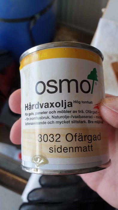 Hand håller en burk Osmo hårdvaxolja 3032, silkesmatt, för träbehandling.