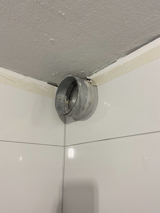 Ventilationsrör som sticker ut från ett badrumstak med vit kakelvägg.