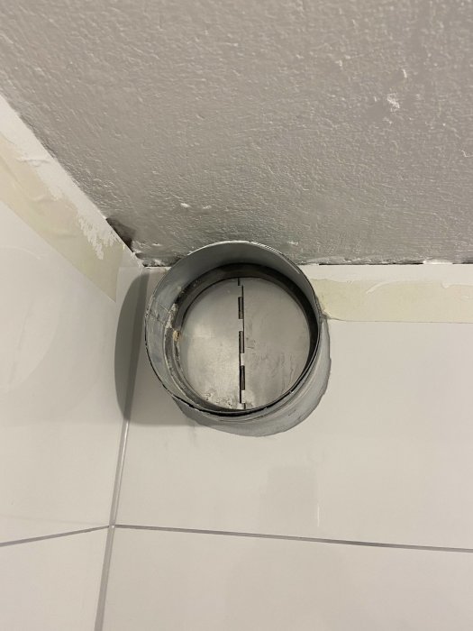 Öppet rör i taket nära en vägg, med spår efter bygg- eller renoveringsarbete.