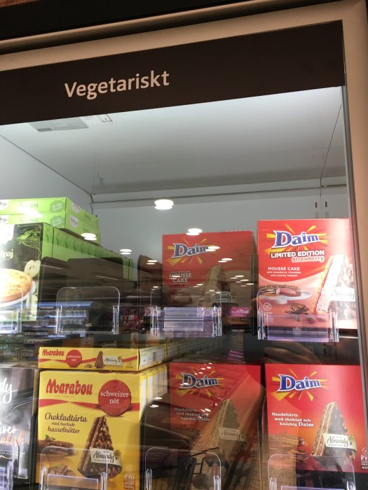 Skylt med texten "Vegetariskt" ovanför ett kylskåp i en affär med chokladvaror istället för vegetariska produkter.