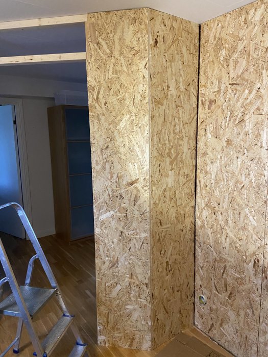 Hörn med nyinstallerade OSB-skivor och en buktning där skivorna inte är helt i linje; arbetsstege syns till vänster.