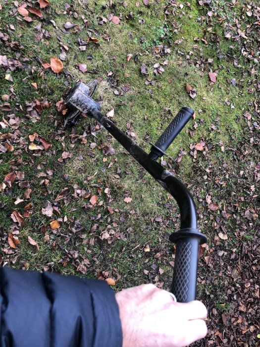 En hand som håller i en kabelläggare med smutsig spade över gräsmark täckt med löv.