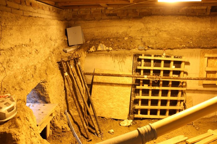 Ongoing basement excavation with exposed pipes, construction shovel, and makeshift wooden supports.