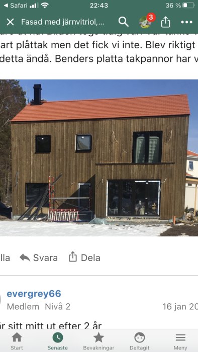 Hus under renovering med träfasad och stora svarta fönster mot en snötäckt mark.