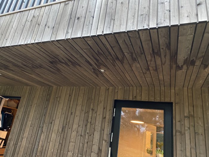 Träfasad och överhäng med synlig fuktskada och mörka fläckar vid ett hörn av en byggnad.
