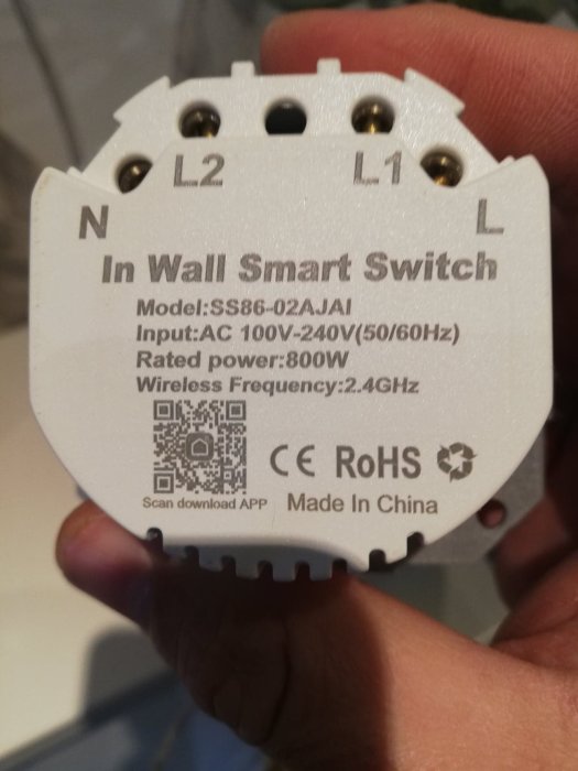 Hand håller en In Wall Smart Switch med märkning för kablage L1, L2, N och QR-kod.