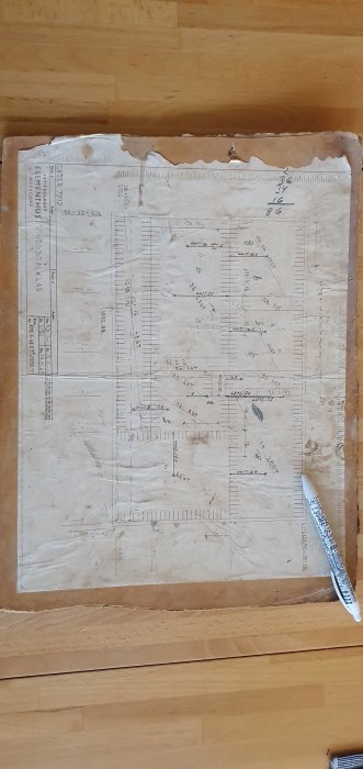 Sliten byggnadsritning för ett 1965 års Mockfjärds Elementhus, utsträckt på ett trägolv.