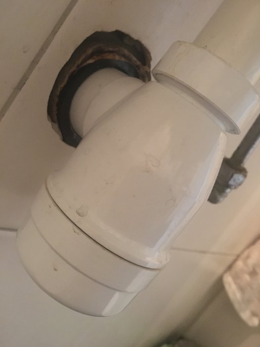 Avloppsrör under handfat med en synlig packning och slitet band där det ansluter till väggen.