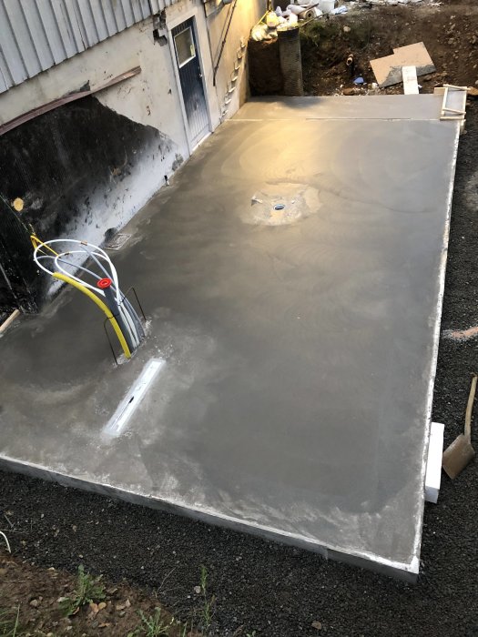 Nyligen gjuten betongplatta med synlig golvränna och armeringskanter, i ett byggprojekt.