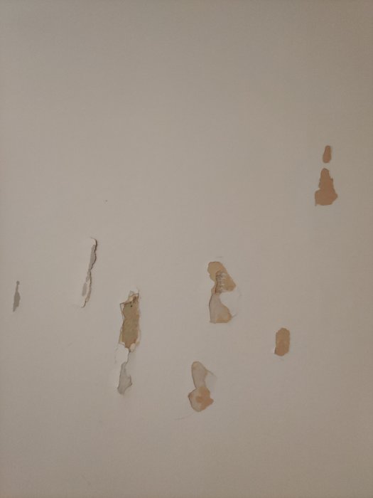 Skadad vägg med flera avslitna områden efter att ha tagit bort självhäftande tejp.