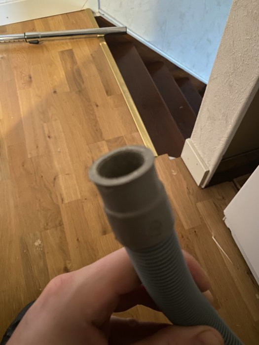En hand håller en flexibel grå slang framför en öppen garderob i ett hem under renovering.