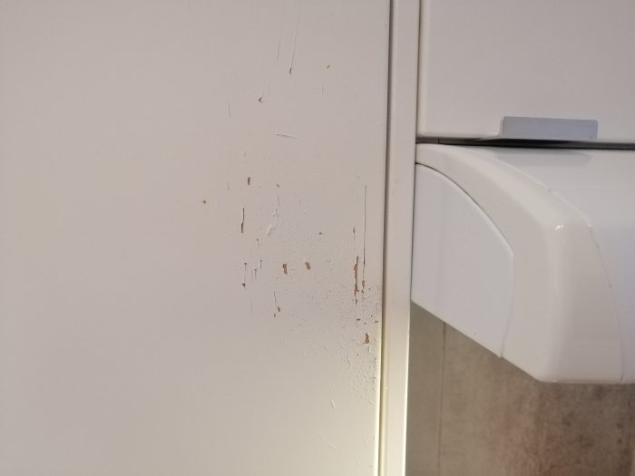 Sliten kökslåda med flagad färg nära vitvaror, tecken på vattenskada och värmeexponering.