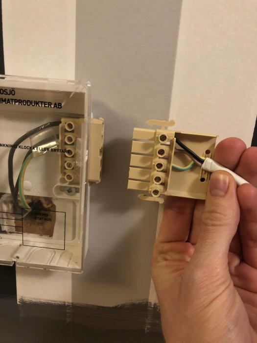 Hand håller skarvkontakt framför kopplingsbox för Gnosjö element med trådar synliga.