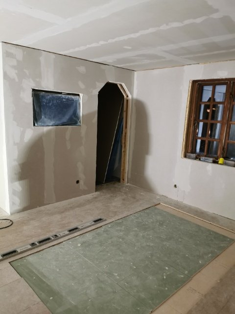 Ett omålade rum under renovering med spacklade väggar, osatt golv och tejp över ett fönster.