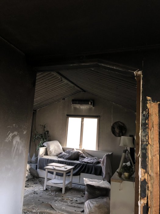 Sotigt rum efter brand med svarttäckta väggar och innertak, skadade möbler och synlig brandskada.