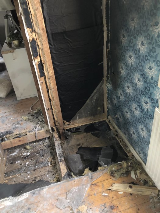 Skadat rum efter brand med exponerade golvbjälkar, förstört golv och avskalade väggar.