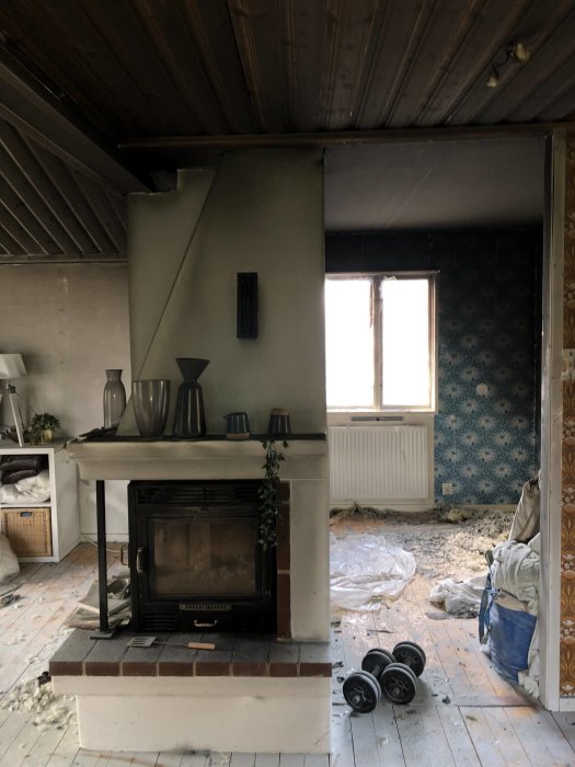 Brandskadat rum med kamin, smält plast, sotiga väggar och rester efter brand i ett fritidshus från 60/70-talet.