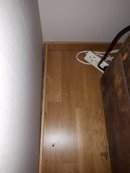 Golvhörn med borttagen list och möjligt gnagspår, eluttag och kablar synliga.