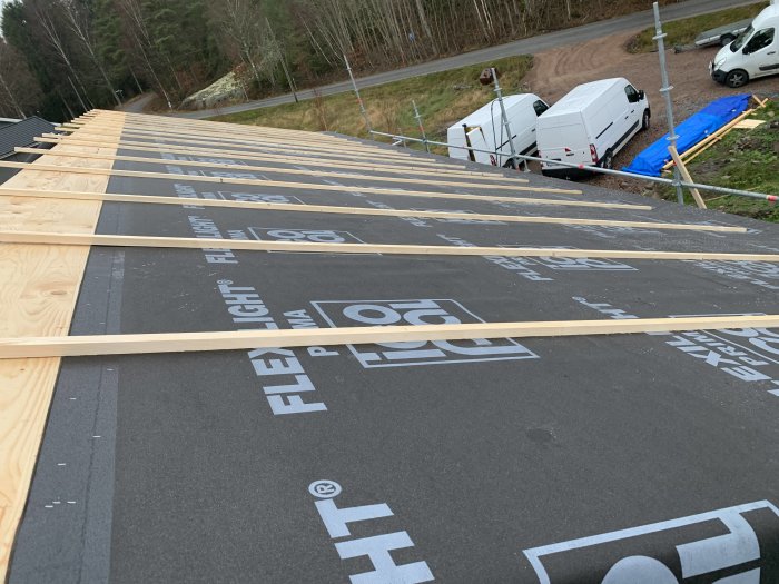 Huset och garaget täckt med skyddsduk och ströläkter, arbetsbilar parkerade i bakgrunden.