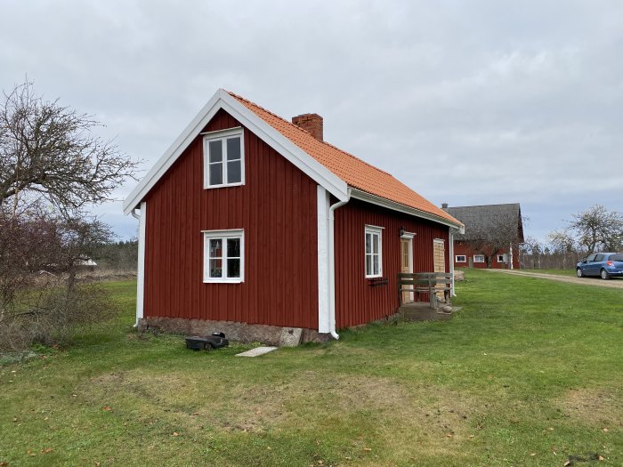 Rödmålat trähus med vita knutar och tegeltak mot en gråmulen himmel.