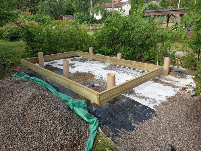 Träram för byggprojekt med borrade hål och jordrör i en trädgård.
