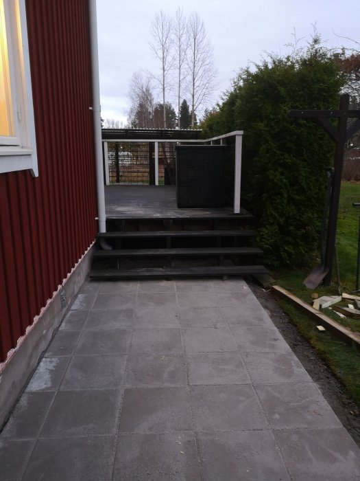 Nybyggd stentrappa och terrass framför ett hus, omgiven av en grön trädgård och klar för soliga dagar.