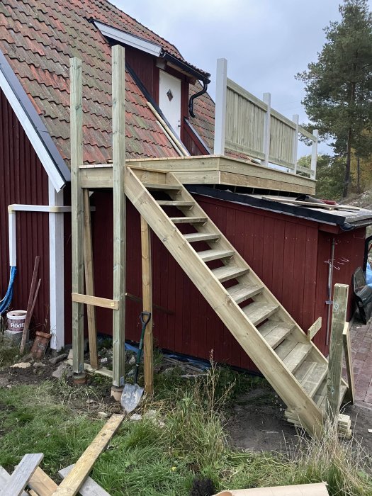 Nylagd trätrappa till en altan på en röd byggnad med omgivande renoveringsmaterial.