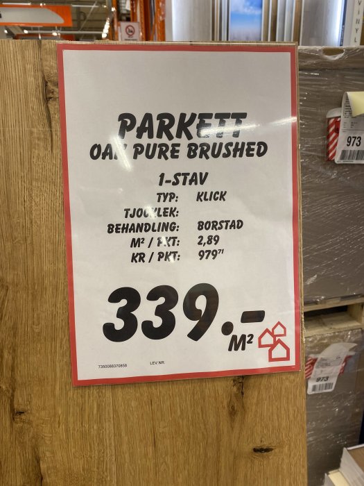 Etikett för parkettgolv med beskrivningen "Oak Pure Brushed", pris och detaljer framför högar av förpackat golv.