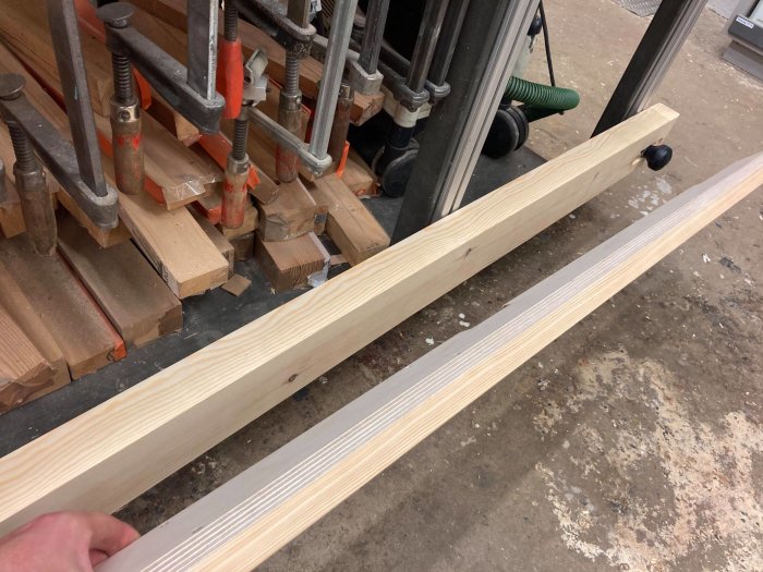 Nytt träbalksskydd med filtyta ännu ej fastlimmad i en verkstad, med hand och arbetsbänk i bakgrunden.