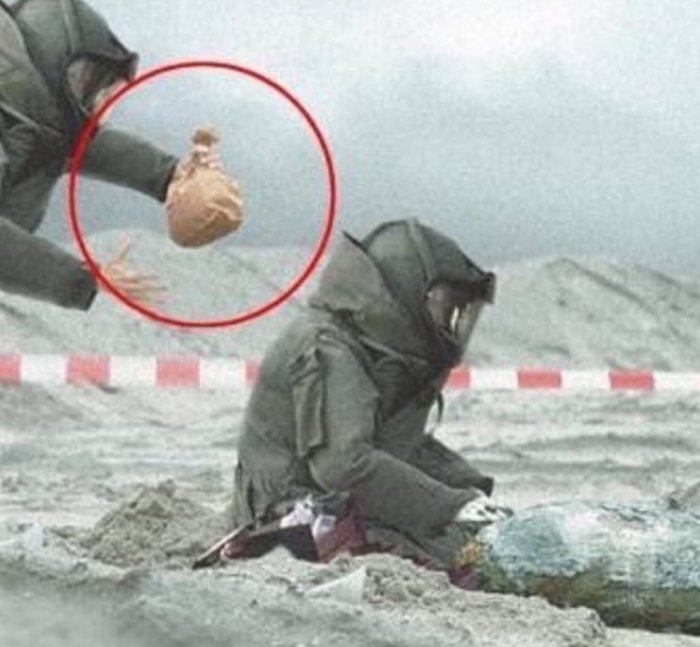 Person i skyddskläder knäböjande vid marken, en annan hand med kruka framför med röd cirkel.