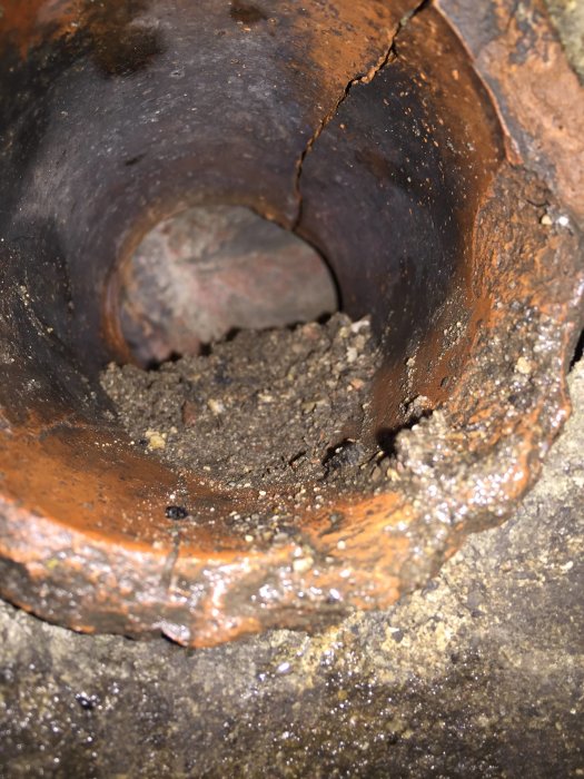 Inblick i rostig, smutsig rörledning med synlig tegelliknande yta och jordrester.