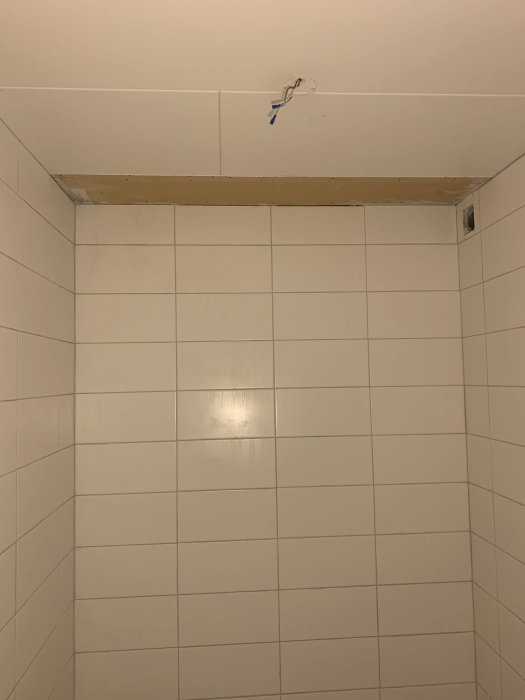 Delvis omålat tak med öppning efter borttagen ventilation ovanför helkaklade badrumsväggar.