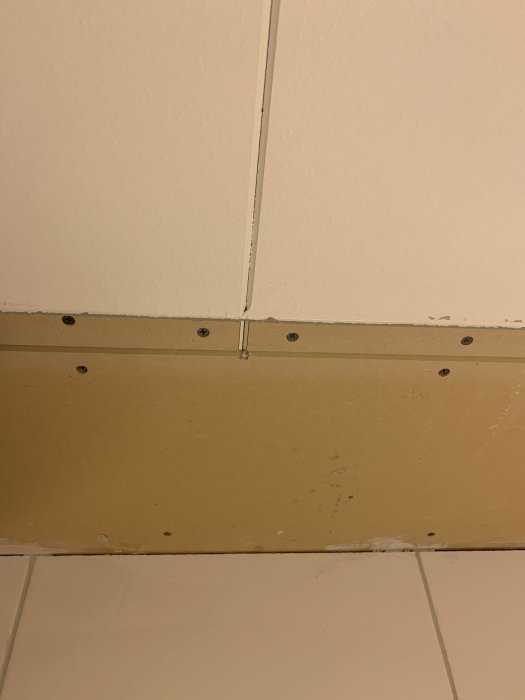 Ommålat tak i badrum med synlig omålad del och spånskiveskiva, i behov av målning eller fuktspärr.