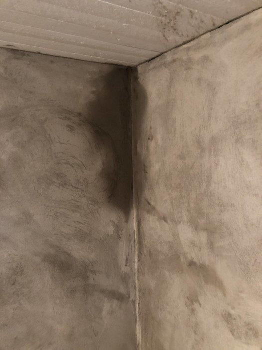 Fuktfläck i ett hörn mellan nyligen putsade väggar i ett rum.