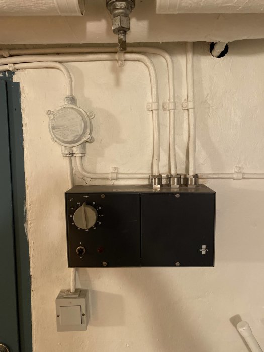 Äldre bastustyrpanel från Bahco monterad på vitmålad vägg med synliga ventiler och rörinstallationer ovanför.
