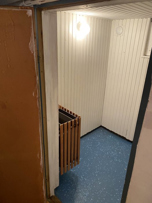 Renoveringsprojekt av bastu med ny vita paneler på väggarna och blåmålat betonggolv, med träribbor staplade i hörnet.