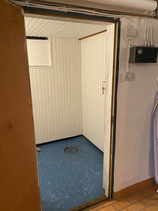 Nypanelad bastu med öppen dörr, blåmålat golv och styrpanel på väggen utanför.