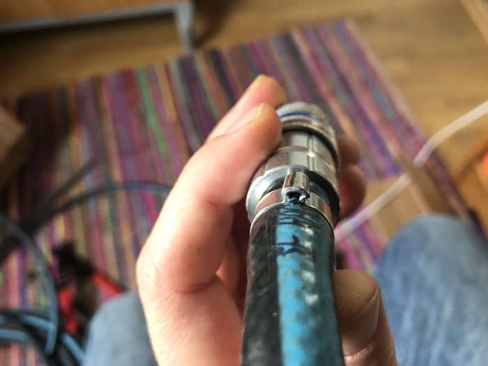 När utsnitt av en hand som håller en 1/2” duabslang med icke plattad öronklämma, med oklar bakgrund.
