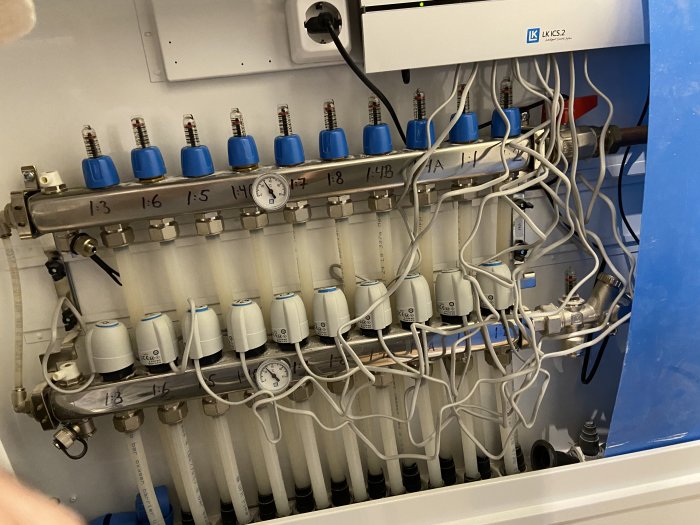 LK värmefördelningsskåp med termostater och rör för golvvärmesystem, manometer synlig.