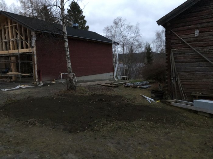 Tidigare plats för elskåp mellan röda och bruna hus med byggmaterial i förgrunden.