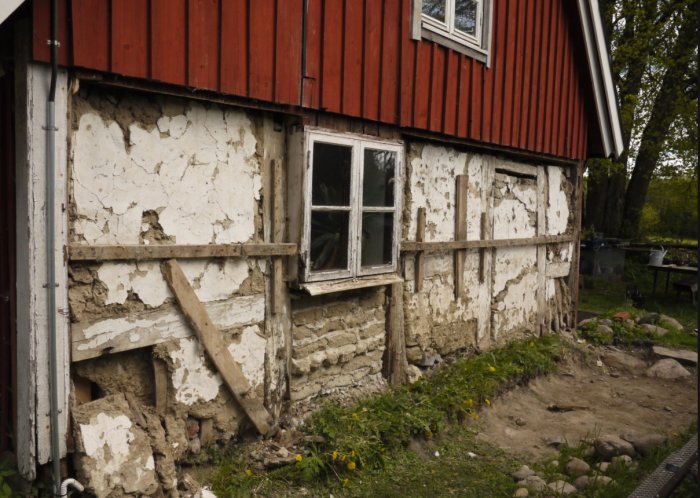 Renovering av fotträ på en gammal skånsk länga med borttagen väggdel och synligt stenfundament.