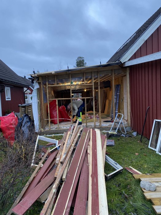 Renovering pågår på ett rödfärgat garage där en vägg reglas om för fönster, med byggmaterial framför.