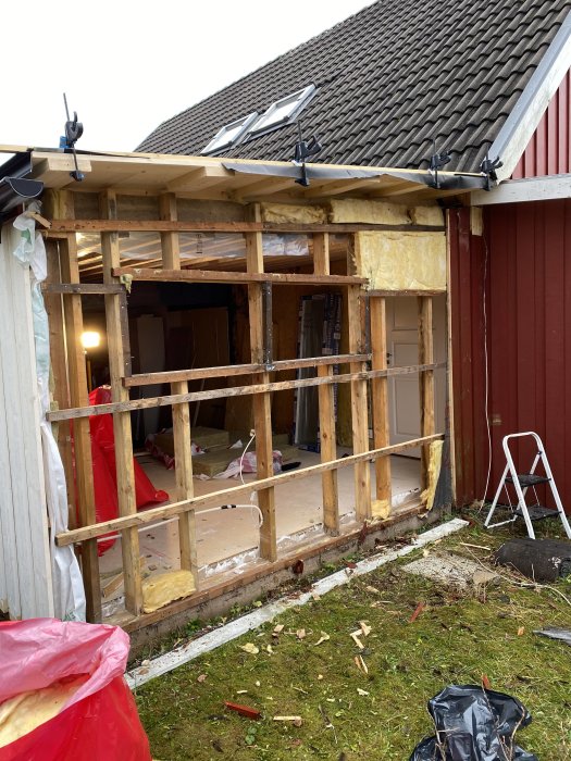 Pågående renovering av ett garage med avlägsnad fasad och ny regelställning för fönsterinstallation.