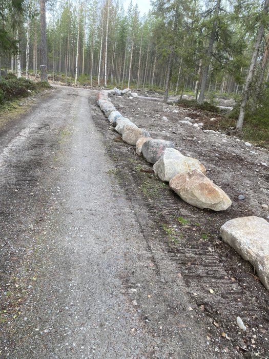 Stenmur längs en grusväg i skogsmiljö som kan blockera åtkomst till fastighet.