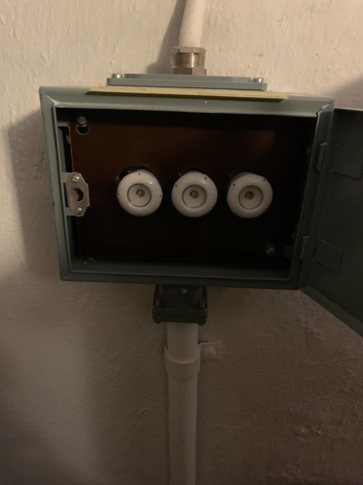 Öppen elanslutningspunkt på vägg med fyra anslutningar och PVC-rör som leder upp till den, i ett hörn av ett rum.