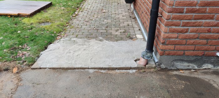 Nyfärdig betongkant vid tegelvägg och sopad fogsand på marken vid stenläggning.