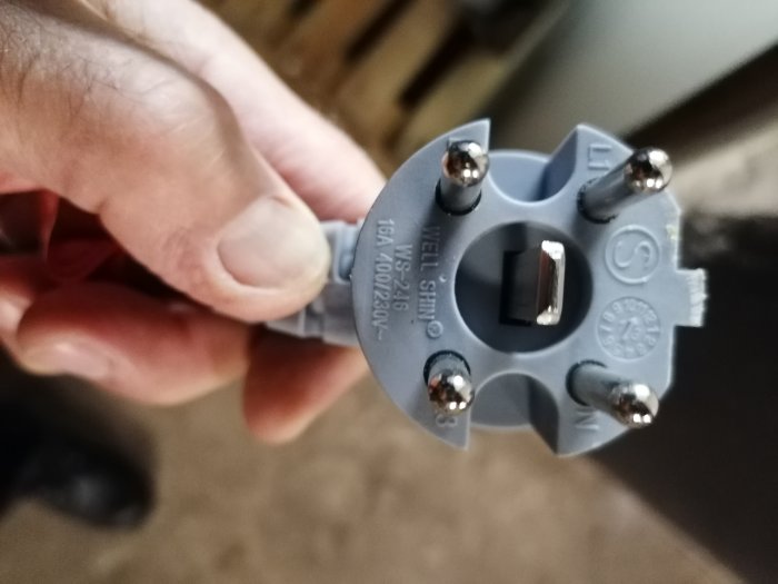 Hand håller en elektrisk anslutning med texten "Max 16A 400V~2,5 6H".