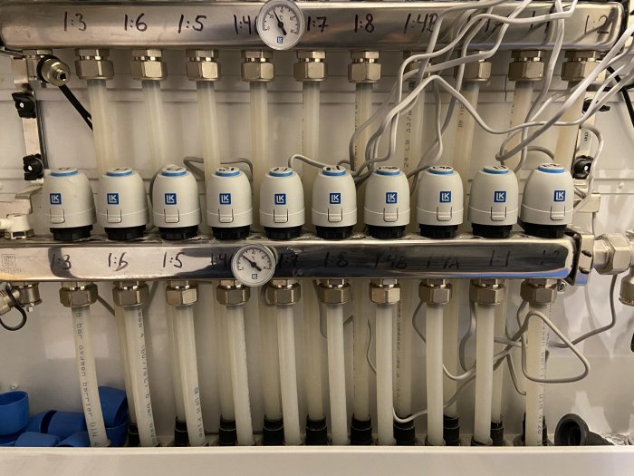 Organiserat värmesystem med märkta ventiler och kablar samt en manometer i ett pannrum.
